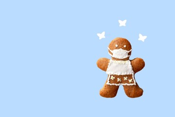 Cute gingerbread woman with protective face mask and butterflies, isolated, blue background. Greeting card, copy space for text. Creative concept in coronavirus (COVID-19) time