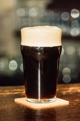 A glass of dark beer on the table in a dark bar. Background bokeh.