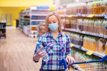 Woman with mask safely shopping for groceries amid the coronavirus pandemic in supermarket. Water selection.