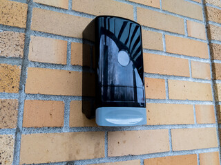 a black plastic hand sanitizer dispenser attached to a red brick wall on the outside of a building