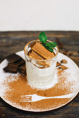 Tiramisu dessert in a glass. silhouette of cocoa fork. classic tiramisu with ladyfinger cookies and mint
