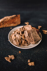 large and small pieces of chocolate. crushed chocolate on a white plate. dark chocolate on a black surface. chocolate macro photo
