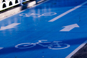 Close up of a blue material covered  bicycle road with double lanes, bicycle icons and direction arrows. 