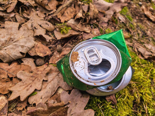 Discarded empty green aluminum beer or soda can lying on dry leaves in the forest