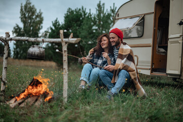 Couple in a checkered plaid roasting marshmallows on fire near the trailer home.