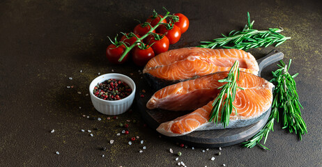 Raw organic salmon steaks with vegetables and spices on dark background close up. Healthy food concept.