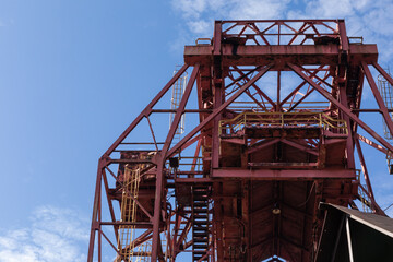 Fototapeta na wymiar Huge rusting overhead industrial metal structure, caged ladders, blue sky, horizontal aspect