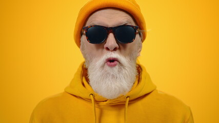 Cheerful elderly man goofing in studio. Mature guy showing tongue indoors.