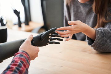 Man holding robotic hand while discussing it with his female client or colleague