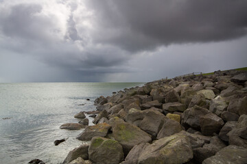 Fototapeta na wymiar Toe protection of a solid sea dike, made of heavy boulders, under dark, threatening sky