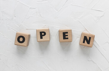 Text OPEN on wooden cubes on white textured putty background.    Square wood blocks. Top view, flat...