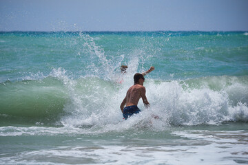 Młodzież aktywnie wypoczywająca w słoneczny letni dzień  nad ciepłym morzem, kąpiele morskie wśród fal.