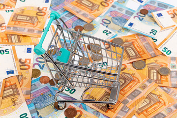 mini shopping cart on the background of euro coins and banknotes, close-up