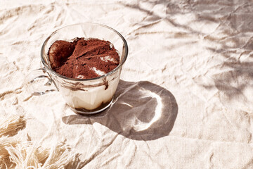 Traditional Italian dessert Tiramisu in a glass cup on a table with linen tablecloth. National cuisine recipe.