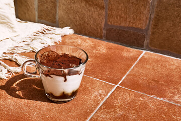Traditional Italian dessert Tiramisu in a glass cup on a tile table. National cuisine recipe.
