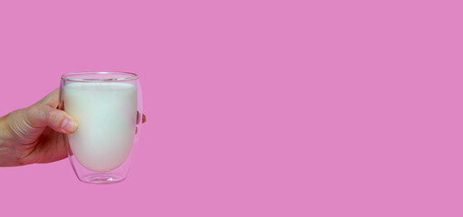 female hand holding a glass with fresh milk, on a pink background,fortified drink, calcium,banner