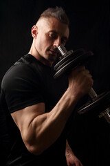 Fototapeta na wymiar Handsome angry strong sporty man doing the exercises with dumbbells on dark black shadow background. Closeup