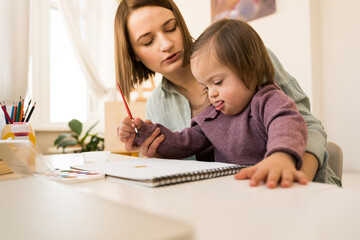 Girl with down syndrome drawing and sitting over a sheet of paper at the table