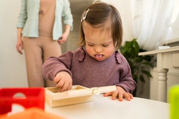Girl with down syndrome standing at the table and playing with her toys