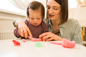 Fototapeta premium Girl with down syndrome sculpturing from the plasticine at the table