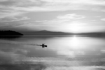 Beautiful sunset at Trasimeno lake with a man on a canoe above perfectly still water