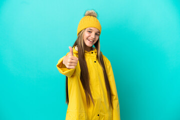 Little girl wearing a rainproof coat over isolated blue background with thumbs up because something...