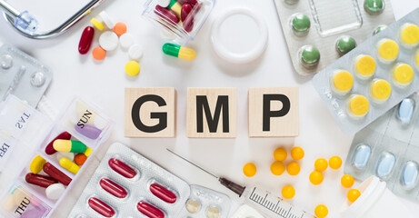 GMP - good manufacturing practice, medicine word on wooden blocks on a desk. Medical concept with pills, vitamins, stethoscope and syringe on the background.