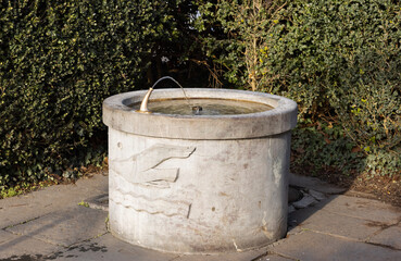 round brown stone fountain with engraved seagull and wavy water, the water tap is in operation, by day, without people