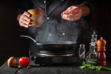 Professional chef pours spices into pan. Steam cooking hot food from a frying pan. Concept cooking process in restaurant kitchen