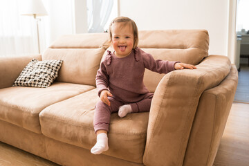 Girl with down syndrome sitting at the sofa and showing her tongue