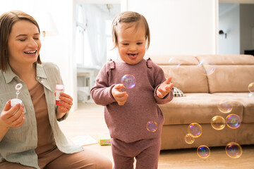 Girl with down syndrome playing with soap bubbles near her mother at home