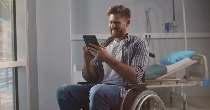 Disabled young caucasian man sitting in wheelchair and using digital tablet