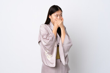 Young Chinese girl wearing kimono over isolated background covering mouth and looking to the side