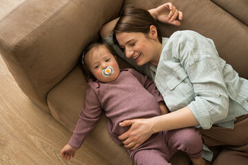 Woman laying at the sofa with her little daughter with down syndrome