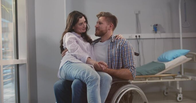 Smiling woman sitting on lap of disabled boyfriend in wheelchair at hospital