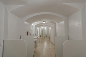 Inside an empty public WC with a white toilet bowl, plumbing fixtures and modern lamps