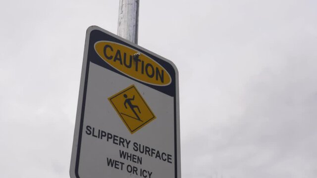 Slippery when wet caution sign at lake front park during cloudy day with grey clouds in the backdrop