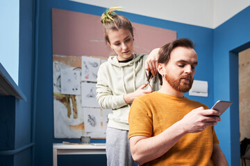 Woman with color hair cutting hair of her bearded man