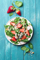 Summer, fresh salad with leafy greens, fresh strawberries, nuts, radishes  and farm cheese on a turquoise wooden background. Healthy food concept