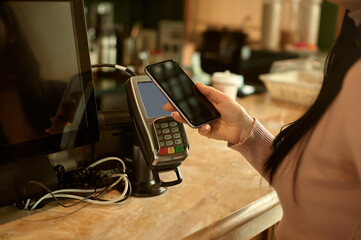 Woman making payment through NFC technology on mobile phone in cafe