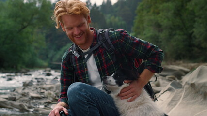 Traveler petting dog at river shore. Redhead man spending time with pet friend