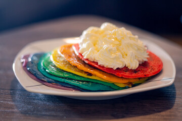 A Plate With A Stack Of Colorful Pancake With Cream On Top