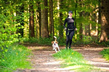 Girl running with dog outdoors in nature on a path in forest.