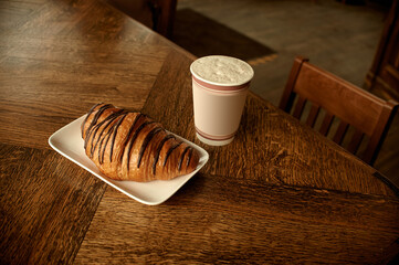 Croissant with coffee to go in a paper cup, take away breakfast