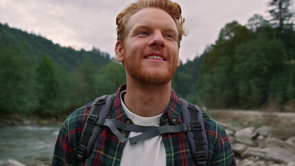 Excited man enjoying hike along river. Guy exploring nature in summer forest