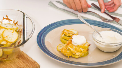 Baked zucchini on a plate close up. Zucchini slices with seasoning salt, black pepper and cheese, served with sour cream.