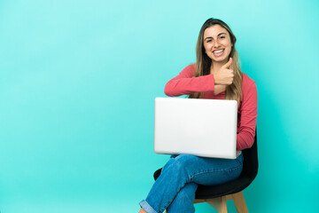 Young caucasian woman sitting on a chair with her pc isolated on blue background giving a thumbs up gesture