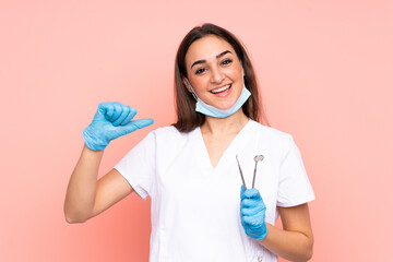 Woman dentist holding tools isolated on pink background proud and self-satisfied