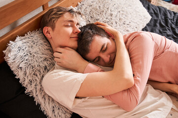 Pleased gay man embracing his boyfriend while laying with him at the bed