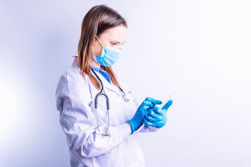 Young caucasian woman with mask gown and stethoscope looking at medical reports on a tablet point concept medicine and technology connectivity